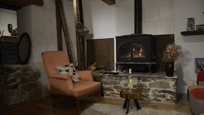 A cozy living room with a stone fireplace, a comfortable armchair, and a small wooden table with a bottle and glasses. - Les Chatougoulis (Bordes-Uchentein)