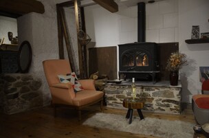 Una sala de estar acogedora con chimenea de piedra, un sillón cómodo y una pequeña mesa de madera con una botella y copas.