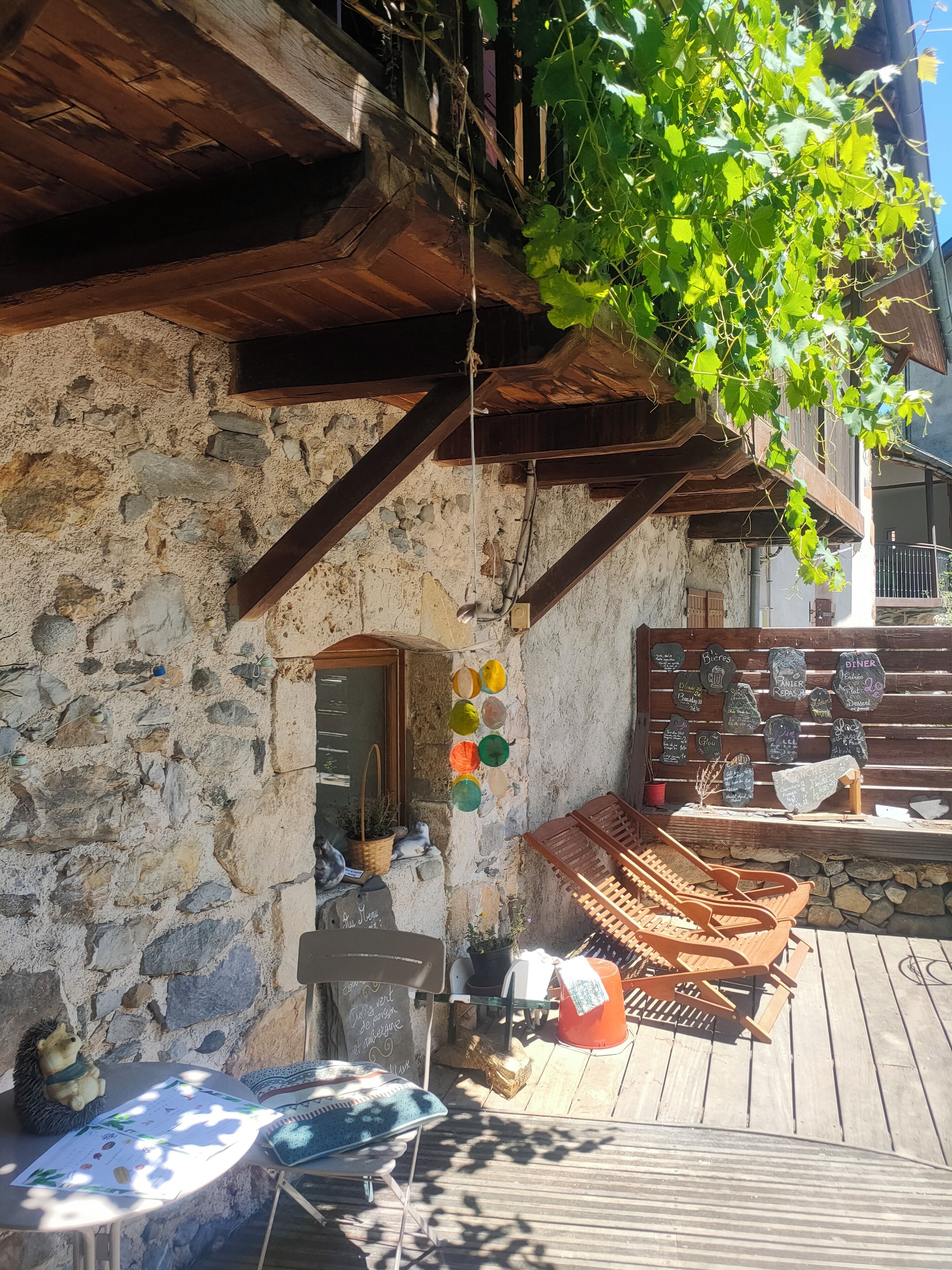 A rustic stone building with wooden beams, a wooden deck, and a hanging plant.