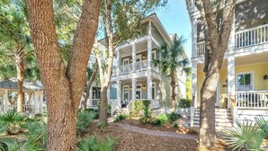A two-story building with a balcony and a porch, surrounded by trees and plants.