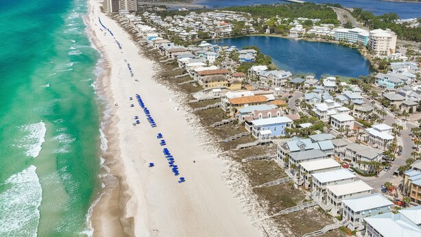 An aerial view of a coastal area with a beach, a marina, and residential buildings.