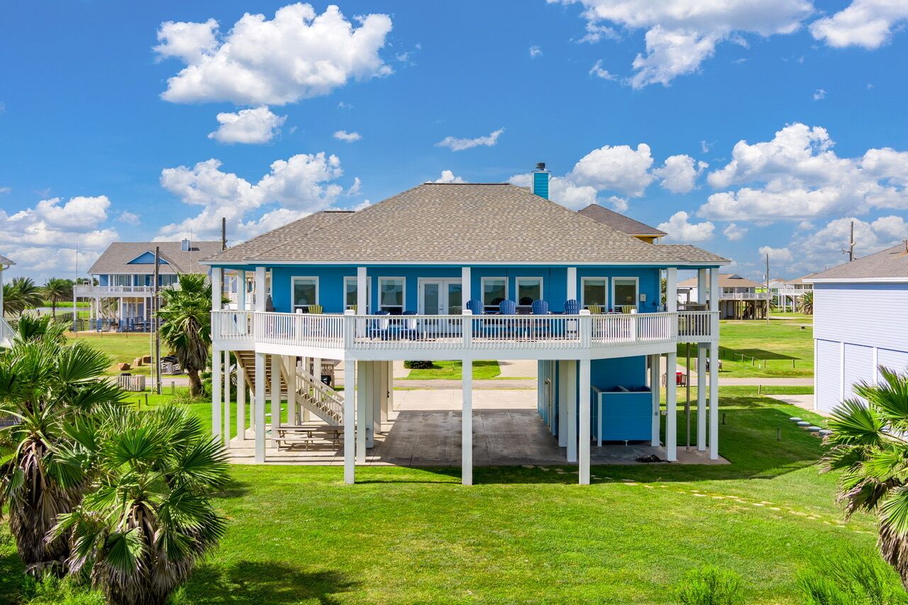 A two-story house with a balcony, surrounded by palm trees and a clear sky.