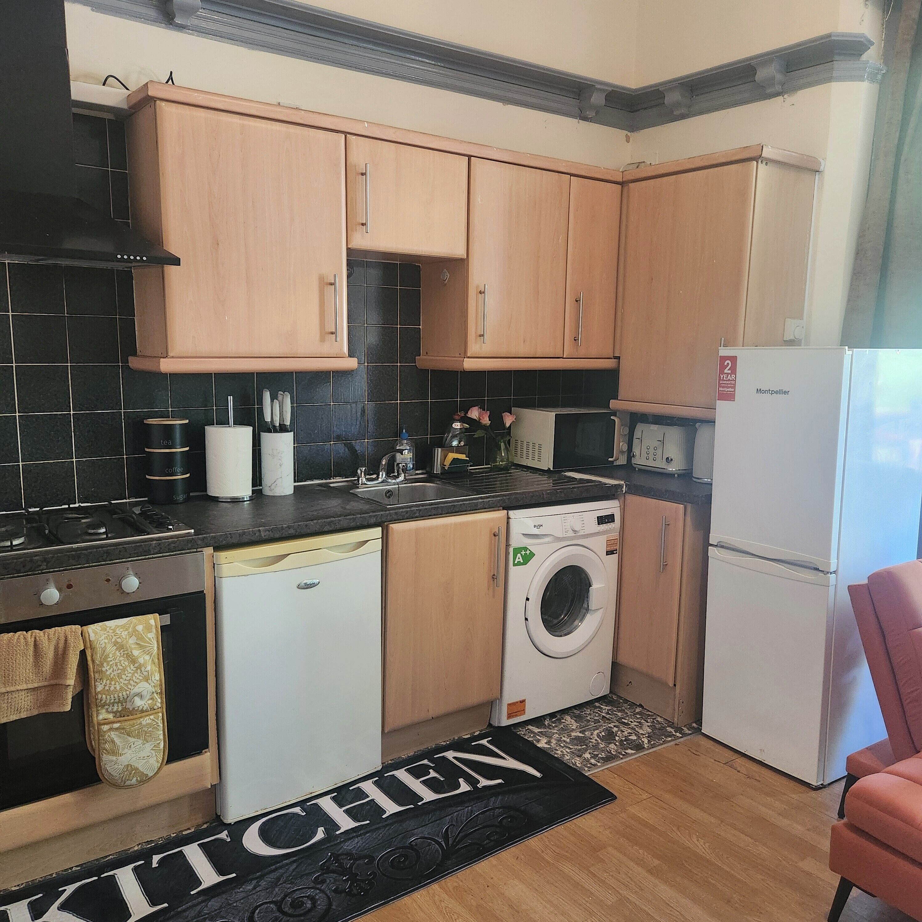 A compact kitchen with wooden cabinets, a dishwasher, a washing machine, and a refrigerator.