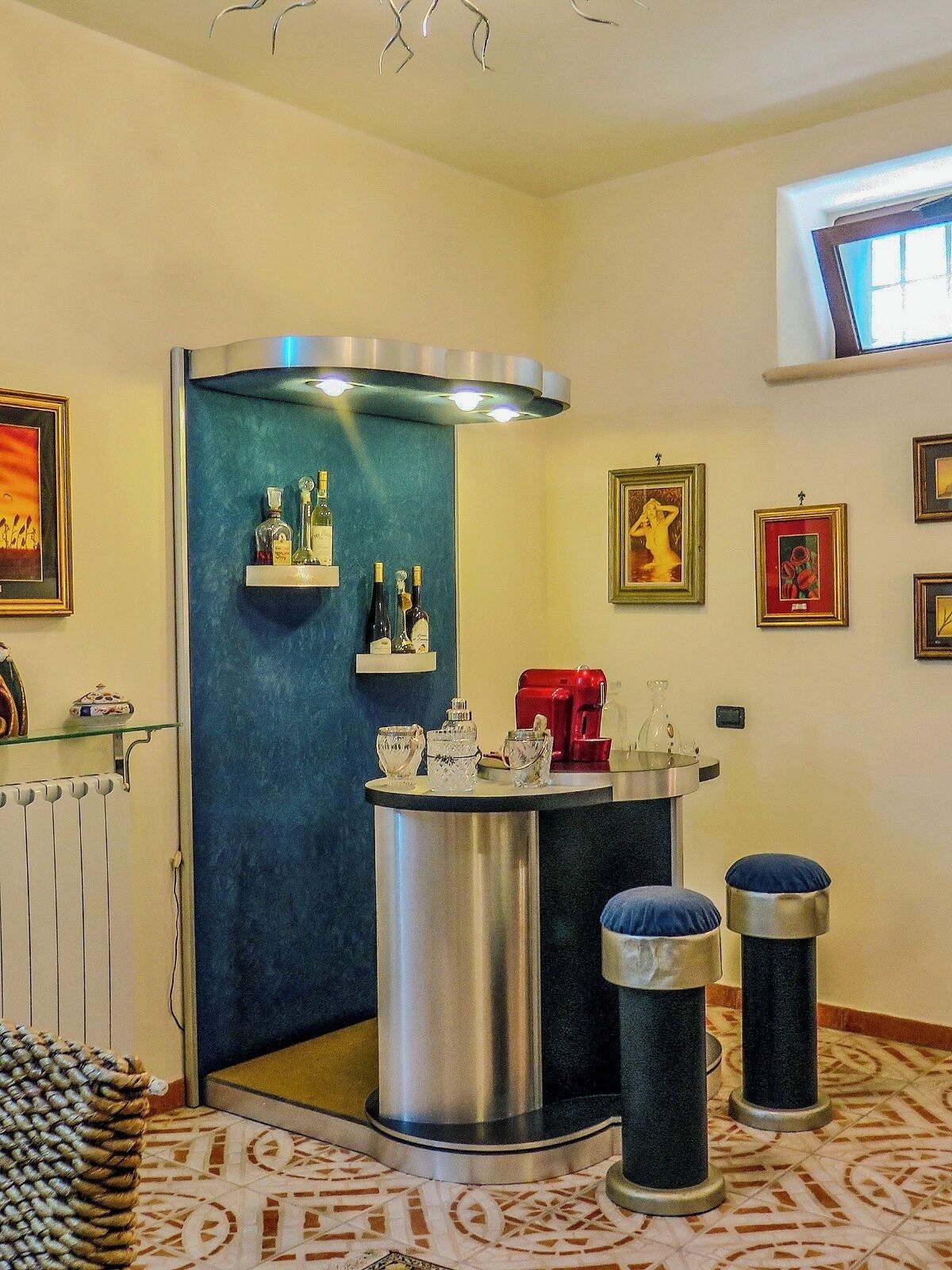 Una habitación de esquina con una pared azul de acento, un objeto cilíndrico metálico, dos taburetes y obras de arte enmarcadas en las paredes.
