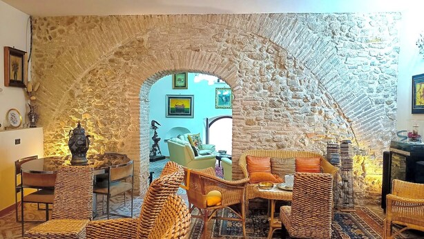 Un interior acogedor con un arco de piedra que conduce a una habitación luminosa, mobiliario de mimbre y un comedor.