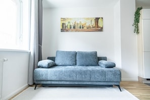 A modern living room with a grey sofa, a cityscape painting on the wall, and a white cabinet with a plant.