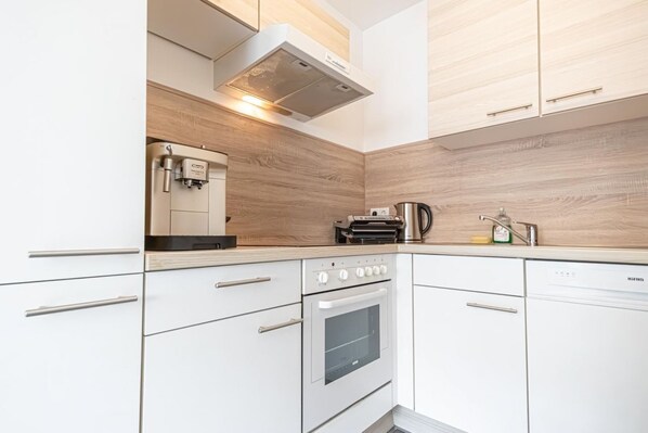 A modern kitchen with white cabinetry, a built-in oven, a coffee machine, and a kettle on the countertop.