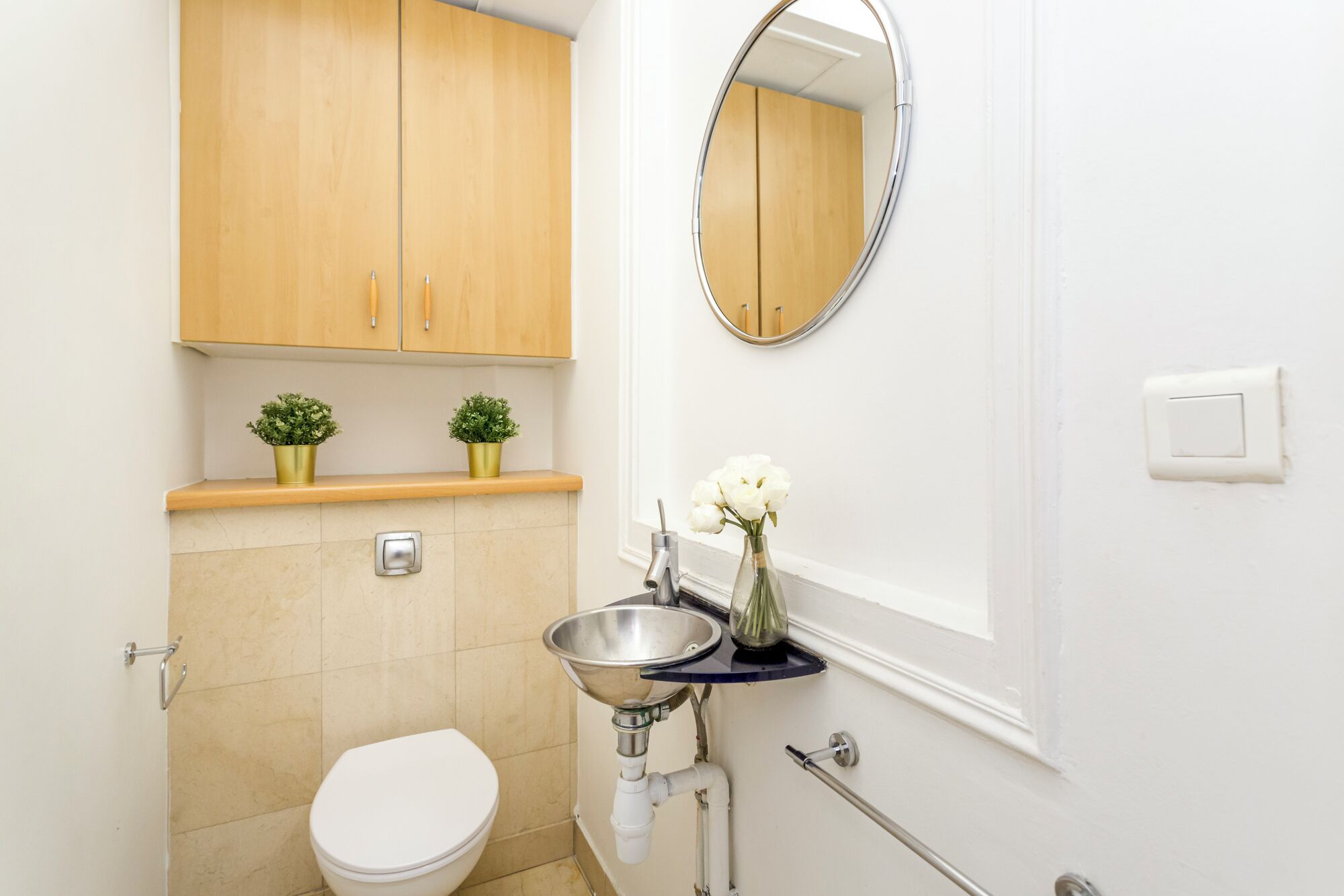 A bathroom with a toilet, sink, mirror, and wooden cabinets.