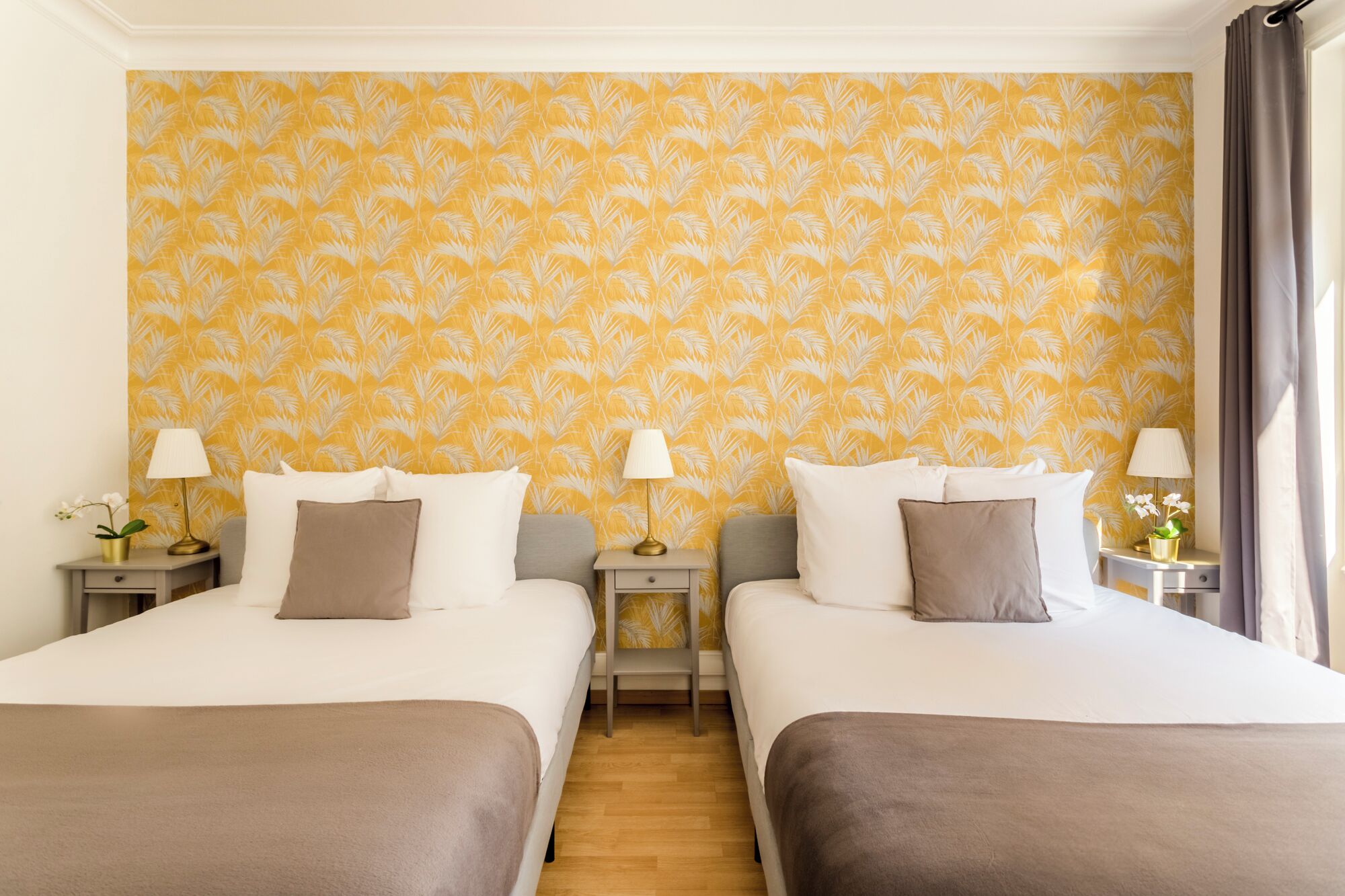 A hotel room with two beds, a wooden floor, and a yellow patterned wallpaper.