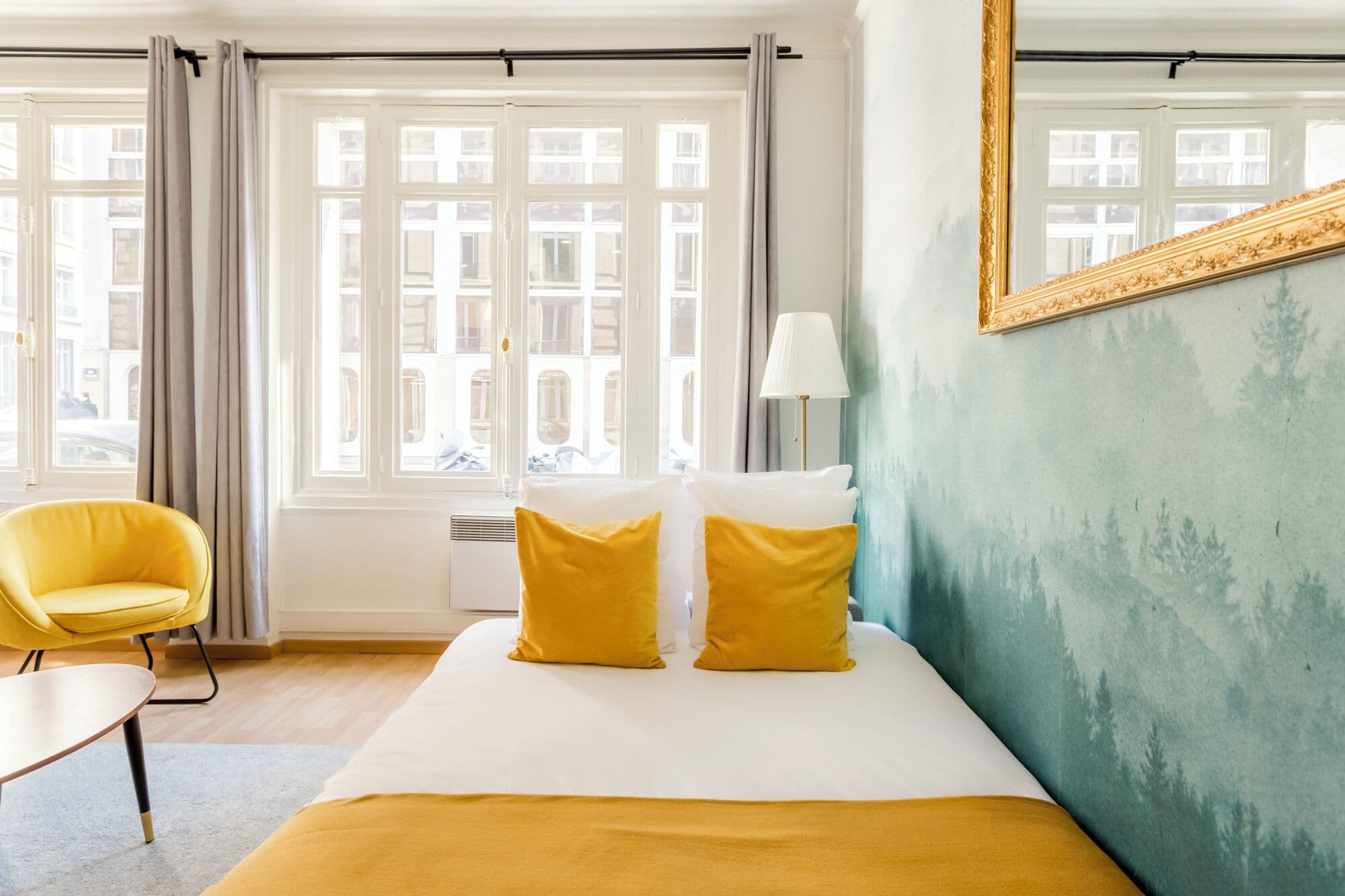A hotel room with a bed, a chair, a lamp, and a large mirror.