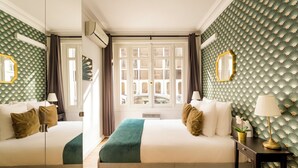 Habitación de hotel con dos camas, un ventanal con vistas a la calle y un papel tapiz estampado.