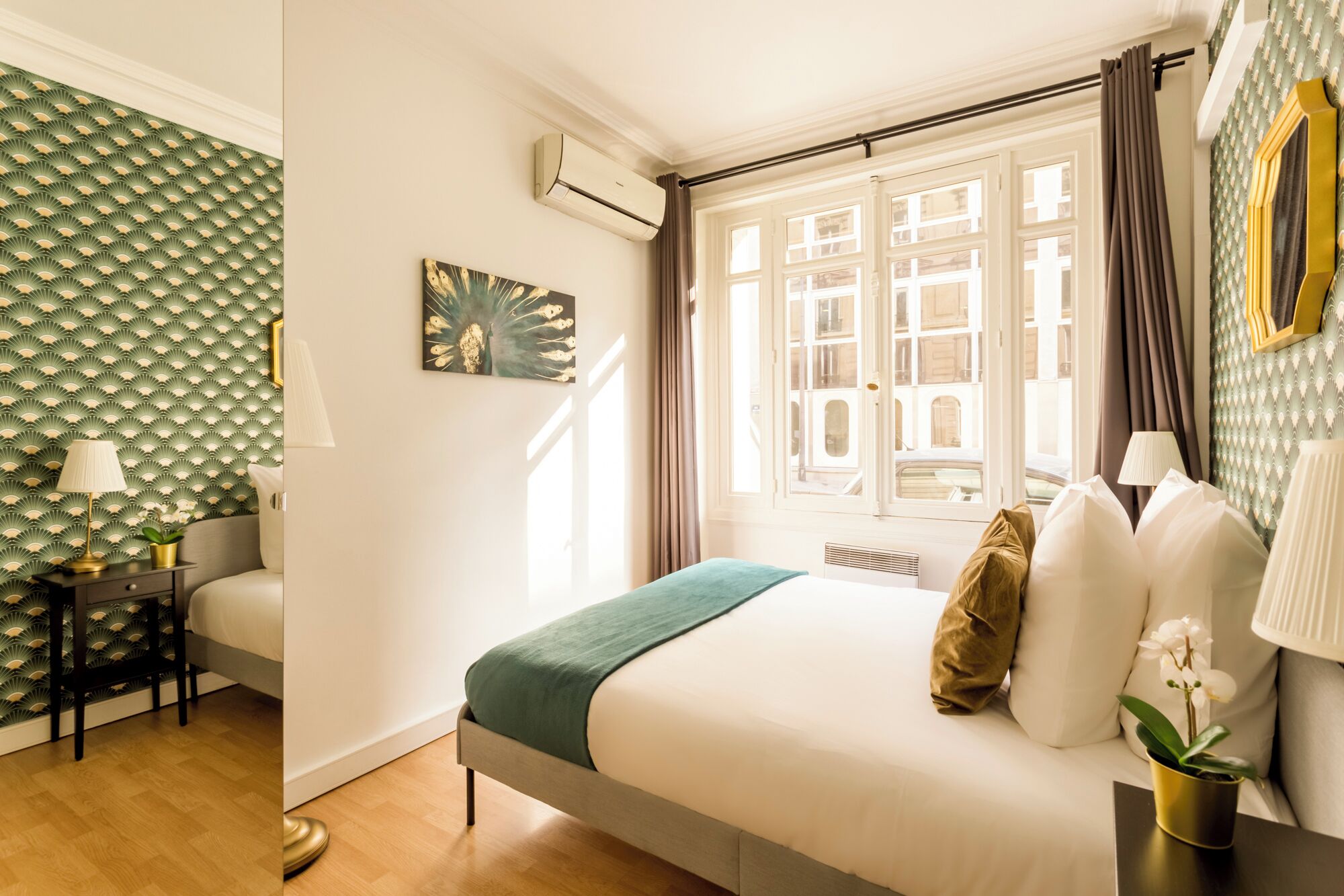 A hotel room with a bed, bedside table, lamp, and a view of the city through a window.