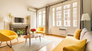 Una sala de estar moderna con chimenea, sillones amarillos, un sofá y ventanas amplias.
