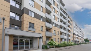 Ein mehrstöckiges Wohngebäude mit Balkonen, einem verschlossenen Eingangsbereich und einer angelegten Grünfläche mit Blumen.