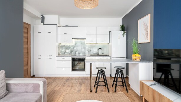 Eine moderne Küche mit weißen Schränken, einem eingebauten Backofen und einer Kochinsel mit Sitzgelegenheiten.