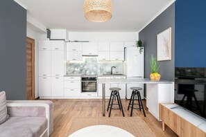 A modern kitchen with white cabinetry, a built-in oven, and a central island with stools. - AS HOME Tęczowa 89 (Wrocław)
