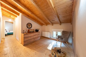 A spacious loft bedroom with a wooden ceiling, a dresser, a chair, and a large window.