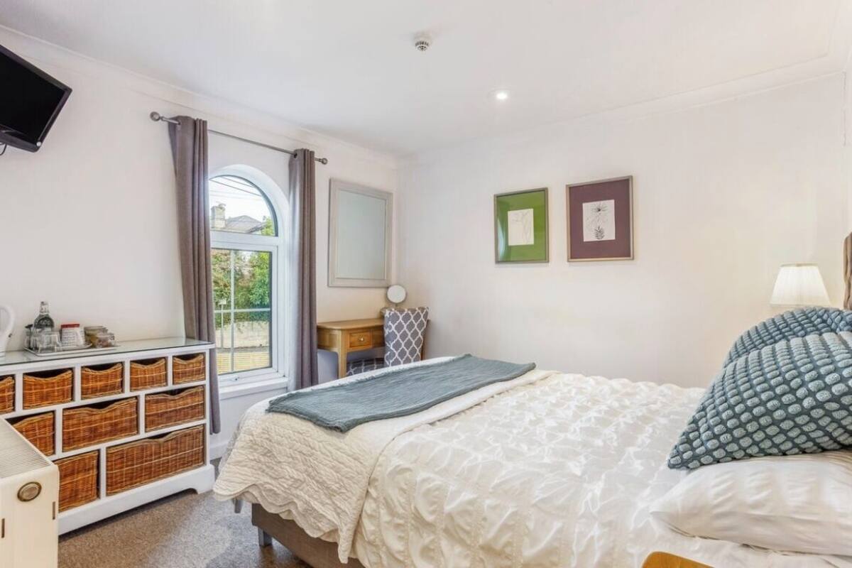 A bedroom with a bed, a dresser with baskets, a mirror, and a window with curtains.