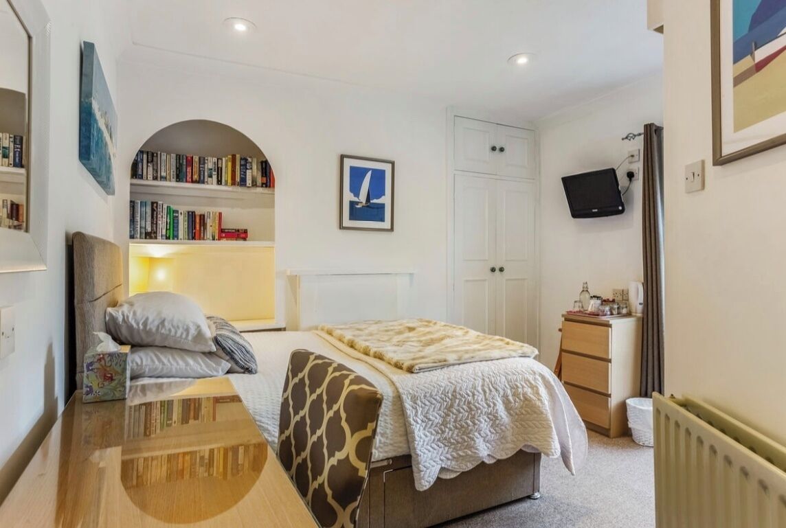 A bedroom with a bed, bedside table, bookshelf, and a TV mounted on the wall.