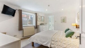 Una camera da letto con un letto, un comodino, una TV a parete, una finestra con persiane e un termosifone.