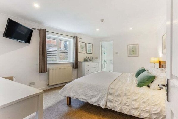 A bedroom with a bed, a bedside table, a TV mounted on the wall, a window with blinds, and a radiator. - Websters Bed & Breakfast (Salisbury)