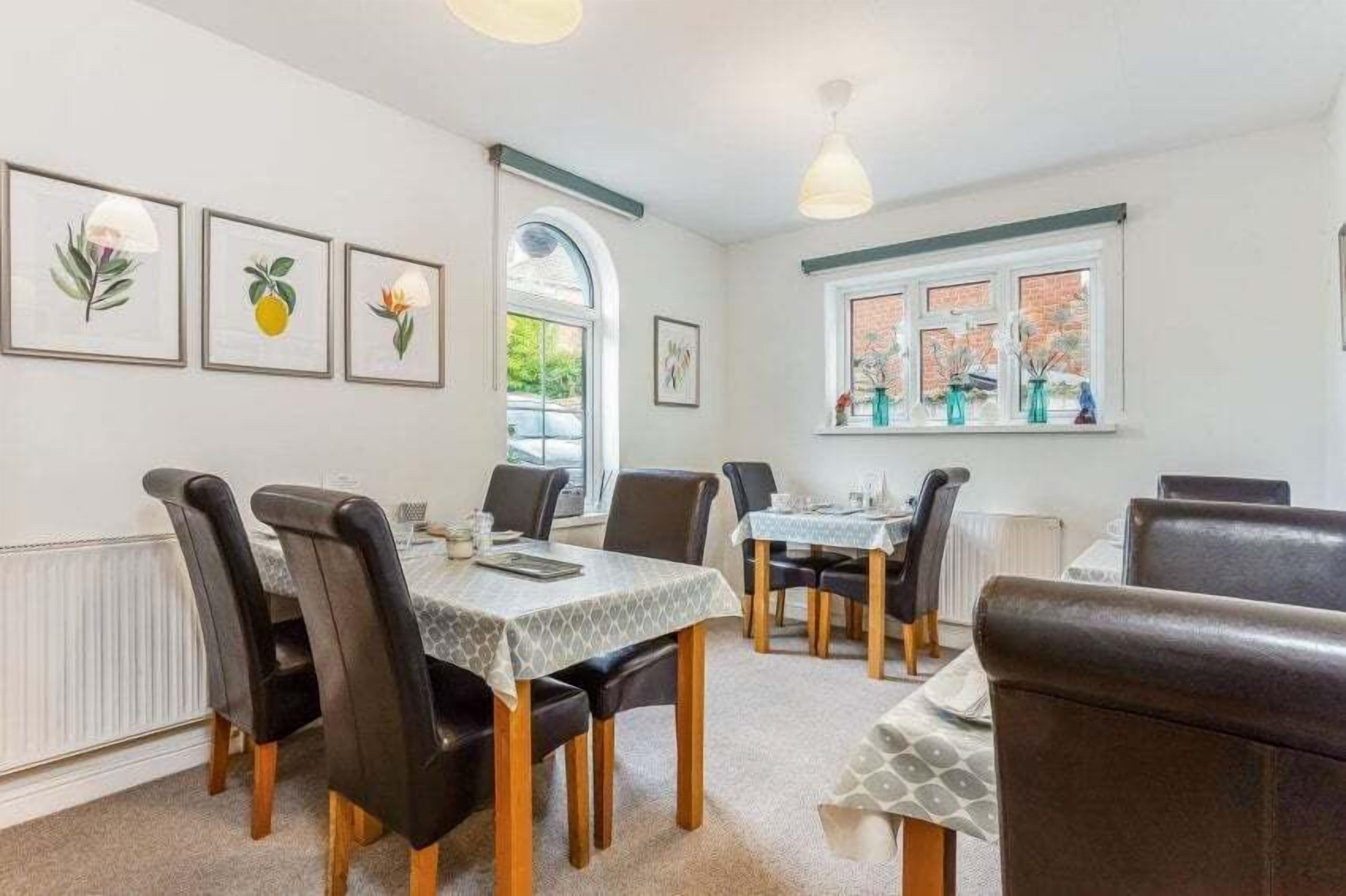 Un coin repas avec une table dressée pour quatre personnes, entourée de chaises, et une fenêtre agrémentée d’objets décoratifs.