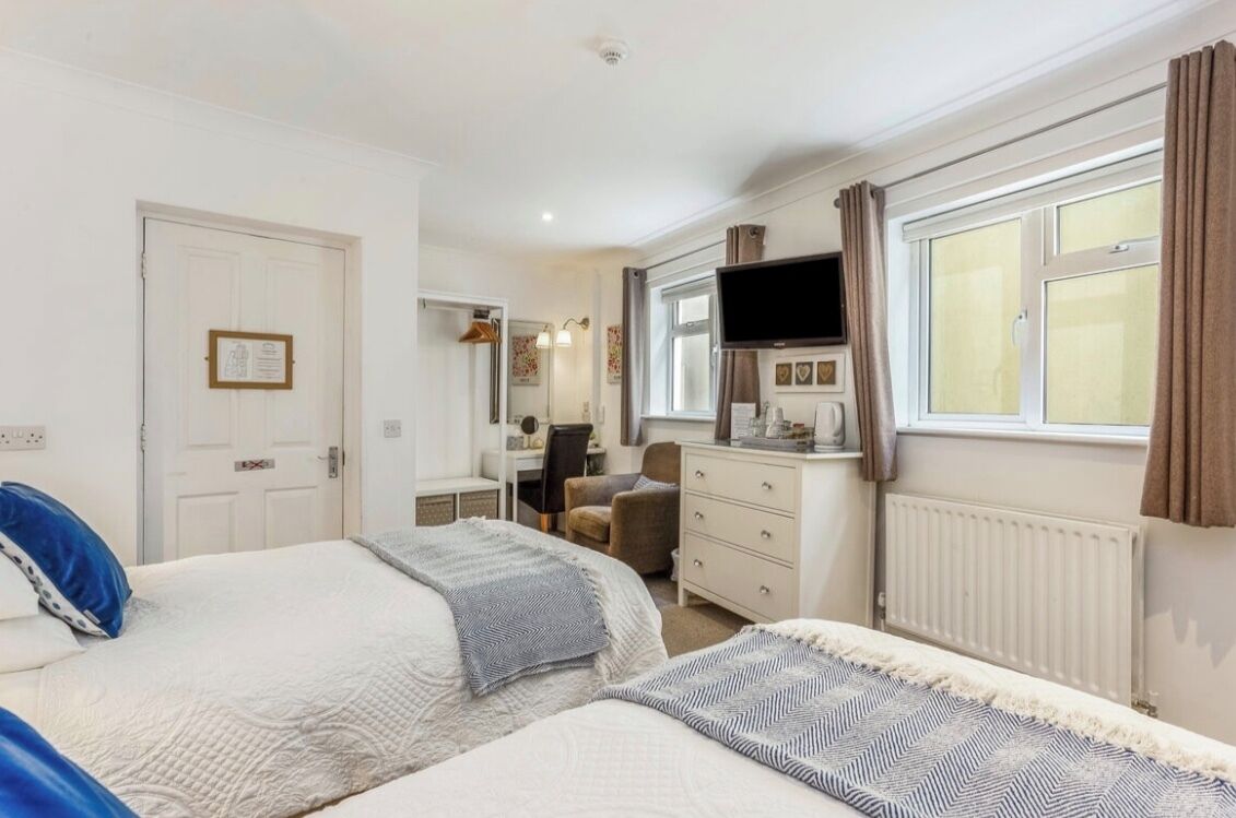 Een hotelkamer met twee bedden, een bureau, een stoel, een televisie en een raam met gordijnen.