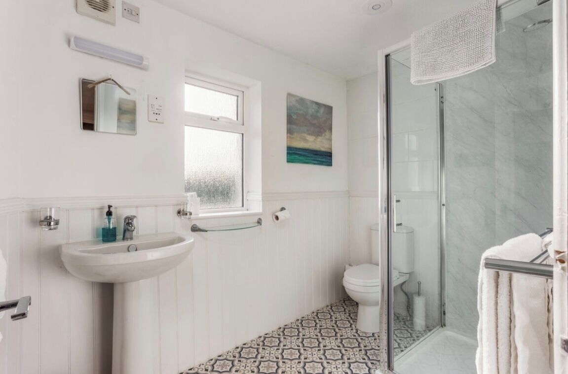 A bathroom with a white sink, a toilet, a glass shower enclosure, and a patterned floor.
