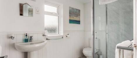 A bathroom with a white sink, a toilet, a glass shower enclosure, and a patterned floor.