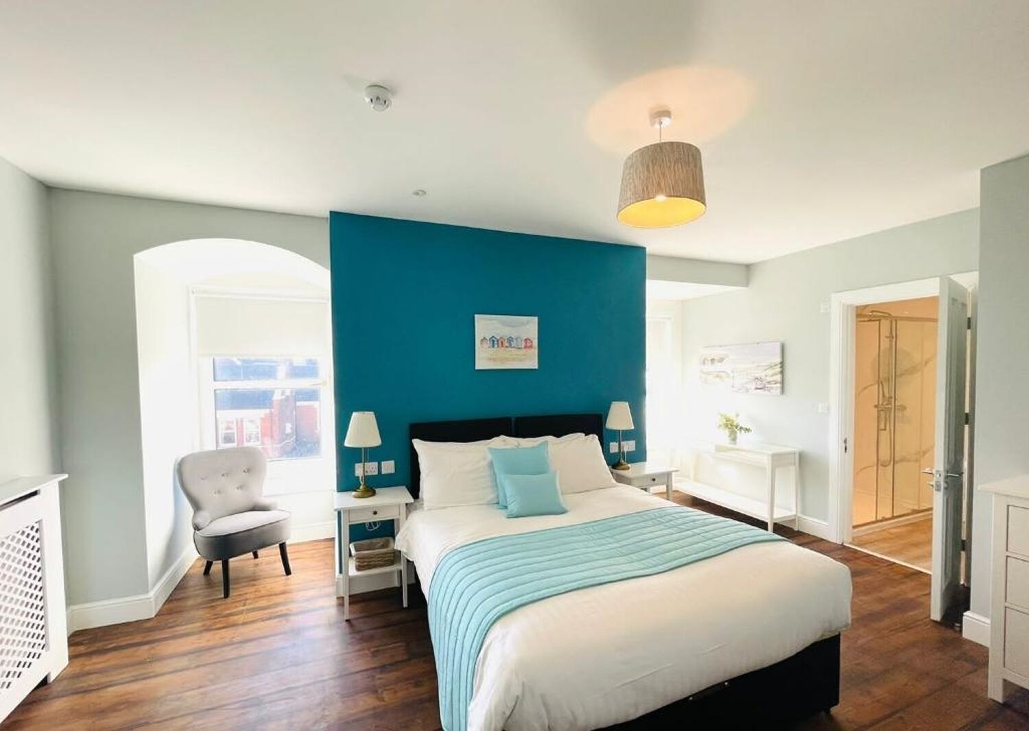 A modern bedroom with a large bed, a blue accent wall, and a view of the city through an arched doorway.
