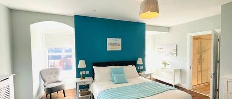 A modern bedroom with a large bed, a blue accent wall, and a view of the city through an arched doorway.