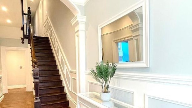 Una escalera de madera oscura con barandillas blancas, que conduce a una plataforma con una mesa consola blanca y un espejo sobre ella.