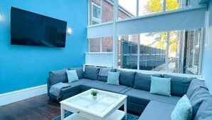 Una sala moderna con un sofá seccional, una mesa de centro de cristal y un televisor grande montado en la pared.