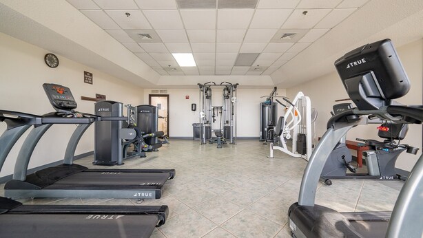 A gym with treadmills, weight machines, and a wall clock. - Phoenix Vi 6609 2 Bedroom Condo (Orange Beach)