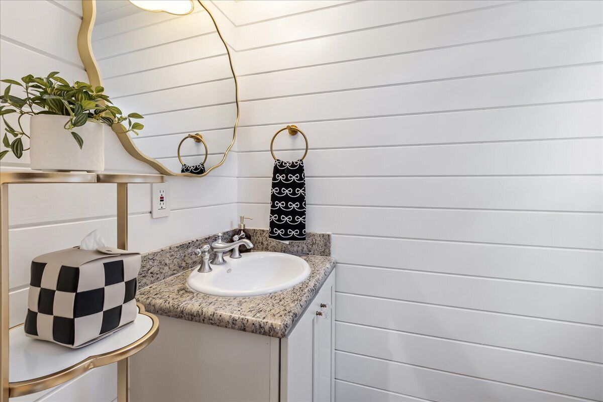 Une salle de bain avec un lavabo blanc, un comptoir en granit, des robinets dorés, une plante en pot, un miroir et un porte-serviettes.