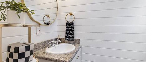 Une salle de bain avec un lavabo blanc, un comptoir en granit, des robinets dorés, une plante en pot, un miroir et un porte-serviettes.