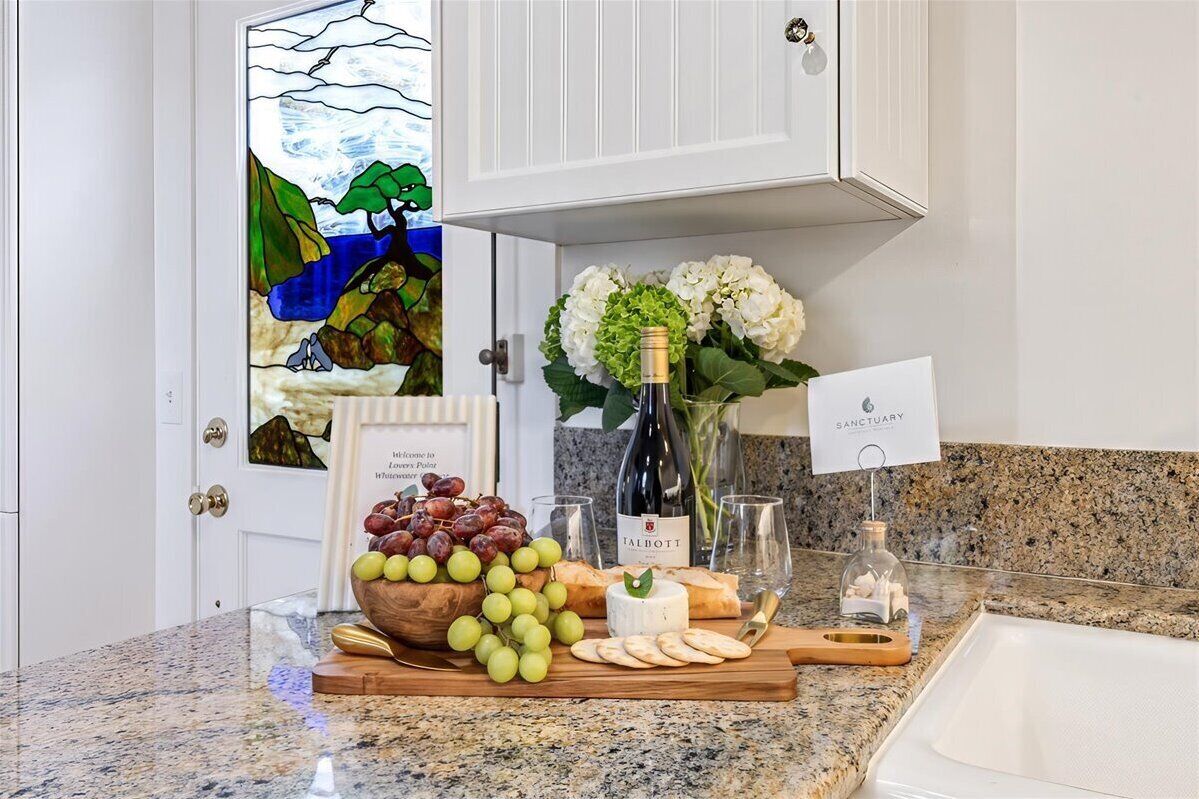 Un comptoir de cuisine sur lequel repose une planche en bois avec des raisins, du fromage et des crackers. On peut également voir une bouteille de vin et un vase rempli de fleurs.