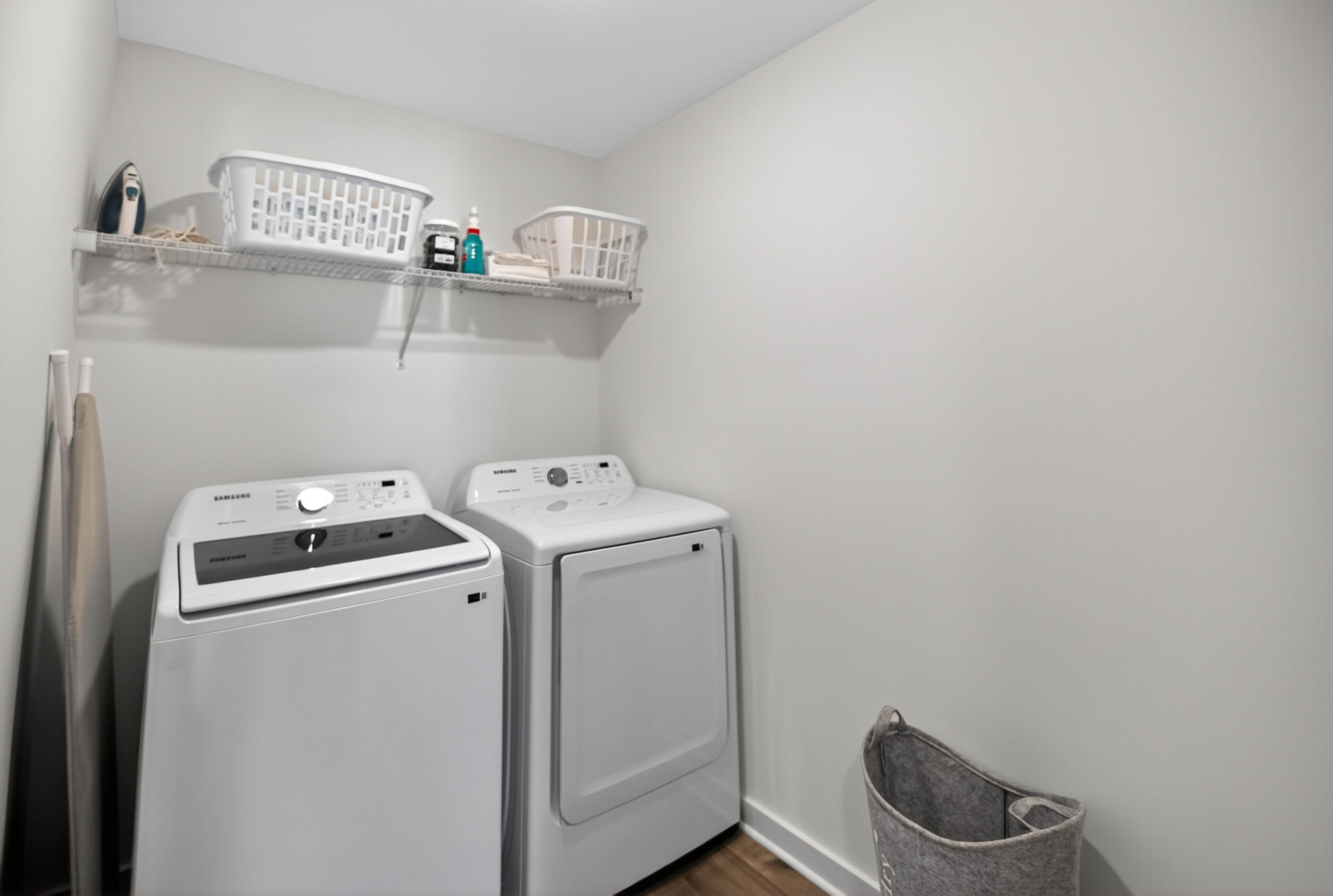 A laundry room with two white washing machines, a shelf with laundry baskets, and a laundry hamper.