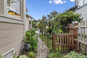 Un étroit sentier mène à une porte en bois, bordée d’une végétation luxuriante et entourée d’un mur de pierre.