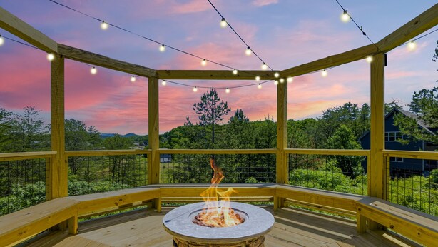 A wooden deck with a fire pit, string lights, and a view of trees and hills. - Smoky Blue Haven 3 Bedroom Cabin (Sevierville)