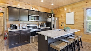 A kitchen with dark cabinets, stainless steel appliances, a granite countertop, and wooden stools. - Smoky Blue Haven 3 Bedroom Cabin (Sevierville)