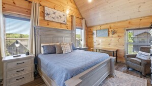 A bedroom with a wooden ceiling, a bed with a headboard, a nightstand, a chair, and a window with blinds. - Smoky Blue Haven 3 Bedroom Cabin (Sevierville)