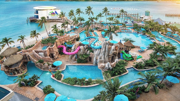 A resort with multiple swimming pools, palm trees, and a beach area. - Margaritaville Waterpark Jacuzzi One Bedroom King Suite (Nassau)