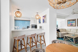 A modern kitchen with bar stools, a dining table, and a living area with a sofa and coffee table.