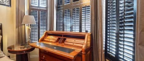 A room with a wooden desk, a lamp, and a bed.