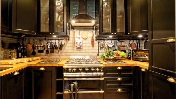 A kitchen with dark cabinetry, a gas stove, an oven, and a countertop with various kitchen items. - Holland Park Classic High Ceilings Luxury 2 Bed (London)