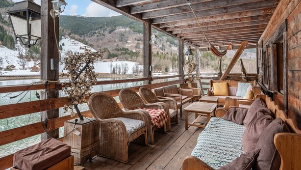 A wooden deck with wicker furniture, a hammock, and a view of a snowy landscape.