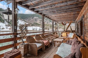 Eine Holzterrasse mit Korbmöbeln, einer Hängematte und Blick auf eine verschneite Landschaft.