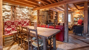 A rustic interior with stone walls, wooden beams, a wooden table, and red seating.