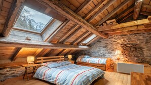 A cozy attic bedroom with two beds, a stone wall, wooden beams, and a skylight.